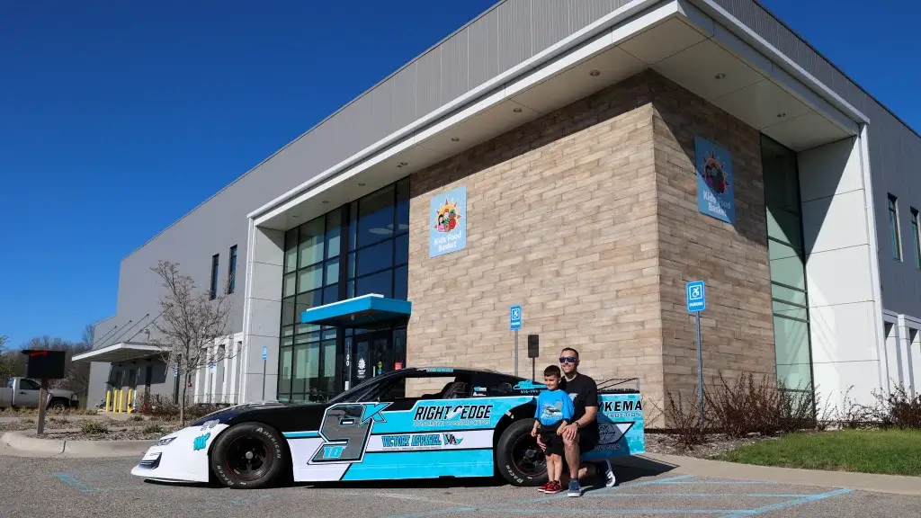 Adam Casari poses for a photo with his son in front of his blue, white and silver race car parked in front of Kids' Food Basket.