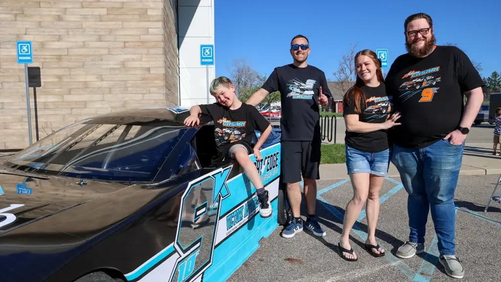 A family pauses for photos with Adam Casari in front of his race car.