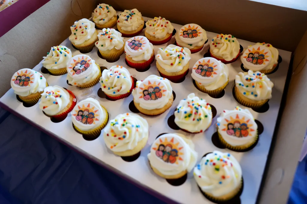 Four rows of white frosted cupcakes alternating with sprinkles and the Kids' Food Basket logo on top.